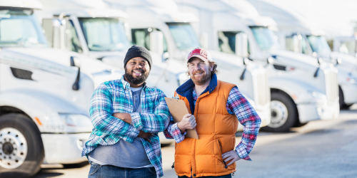 Two men standing in front of a fleet of semi trucks